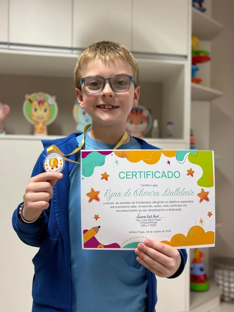Menino sorrindo segurando medalha e certificado de conclusão da fonoterapia